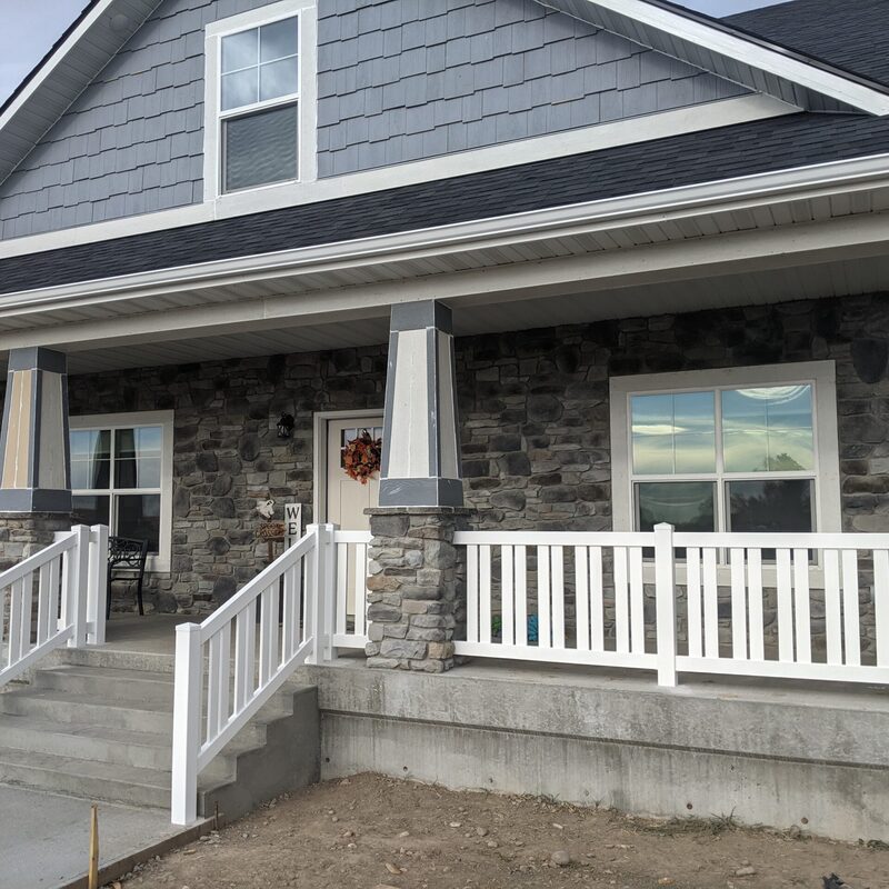 Welcome home with this stunning custom front entry by DeckPro LLC. This comprehensive project integrates a substantial concrete porch foundation and wide, easily accessible concrete steps with high-curb-appeal features. The defining elements are the striking craftsman-style tapered columns, which feature rugged grey stone bases and unique, grey-and-white pinstriped painted wood tops.