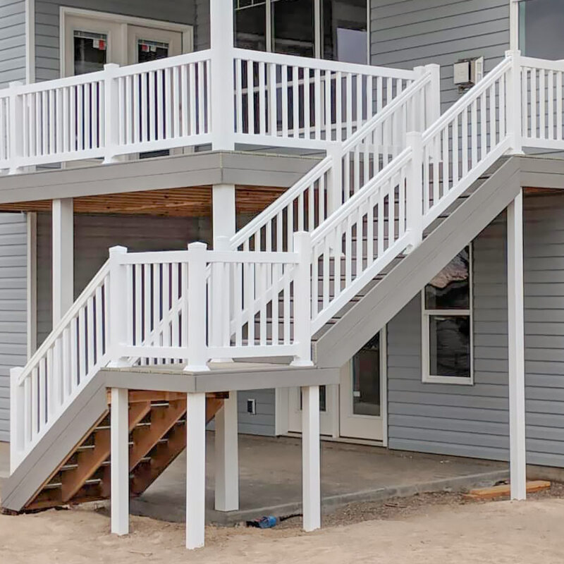 Extend your upper-level living space with this cozy raised balcony deck by DeckPro LLC, which combines rustic elements with modern comfort. We installed low-maintenance composite decking in a warm brown tone and paired it with sophisticated black metal perimeter railings to ensure unobstructed woodland views. Direct access via a white-trimmed glass door makes this sturdy retreat the perfect mountain retreat to take in scenic forest views, pictured here on a sunny day with distinctive shadows cast across the deck boards.